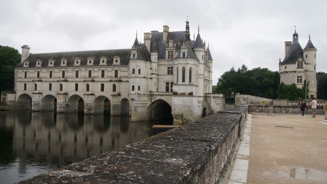 A white stone building with slate roof stands on several arches spanning a river