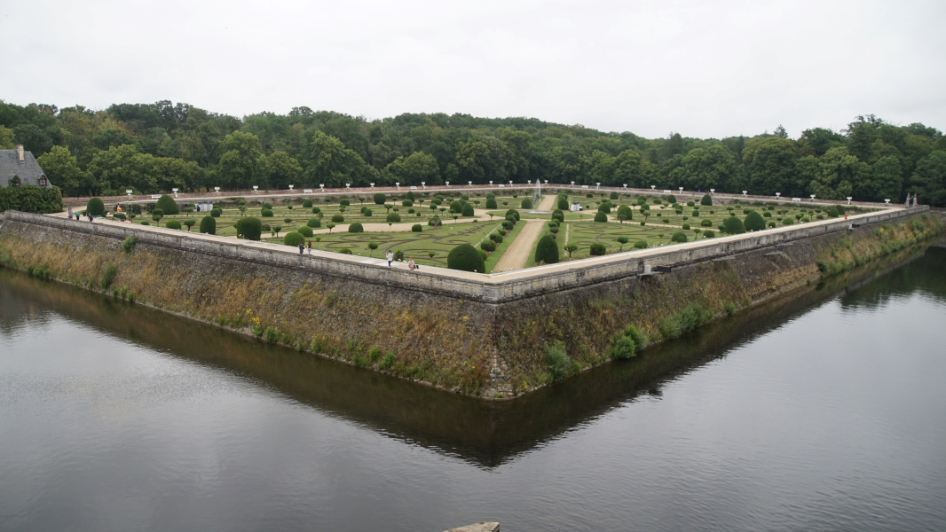 Sloped stone walls separate a river from a formal garden divided by walking paths into eight wedge shaped sections