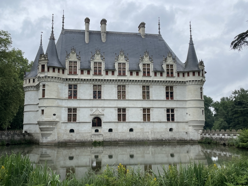 The white walls of a three-story stone building are reflected in a small pond