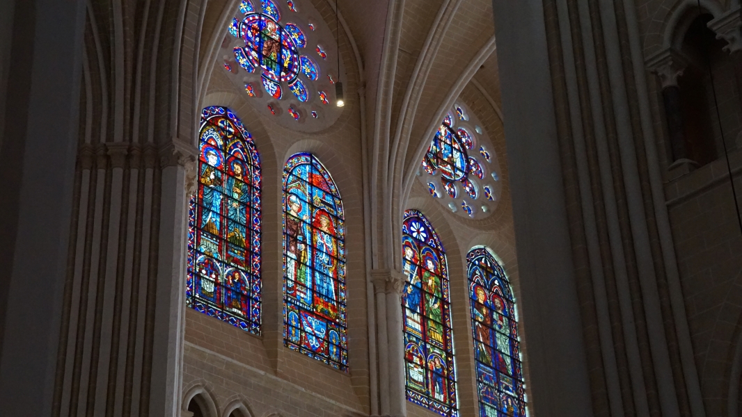 Brightly colored stained-glass windows in warm tan stone walls depict historic figures
