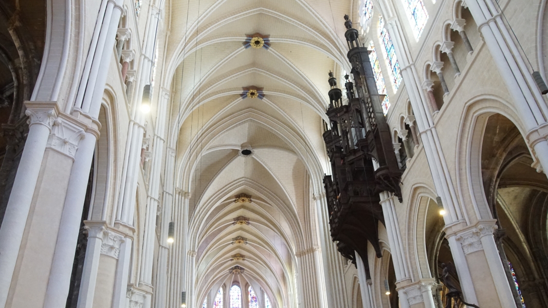 Warm tan and white stone extend to a high ceiling with gothicly detailed columns and a dark wood organ enclosure