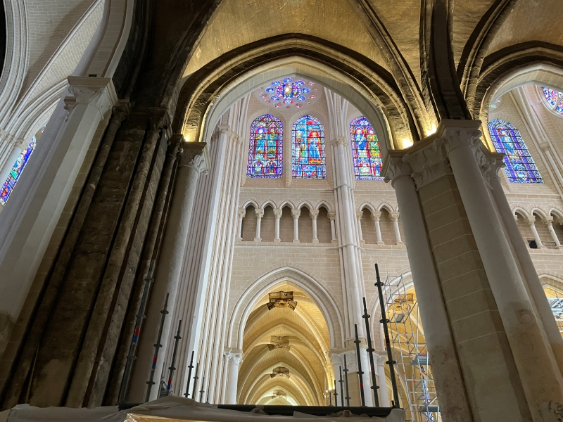A dark stone column extends to a low ceiling with bright stone and stained-glass beyond