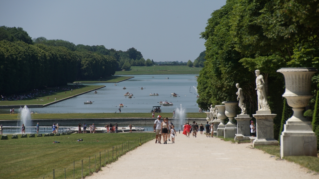 Small row boats dot the surface of a large body of water set between green lawns and manicured trees