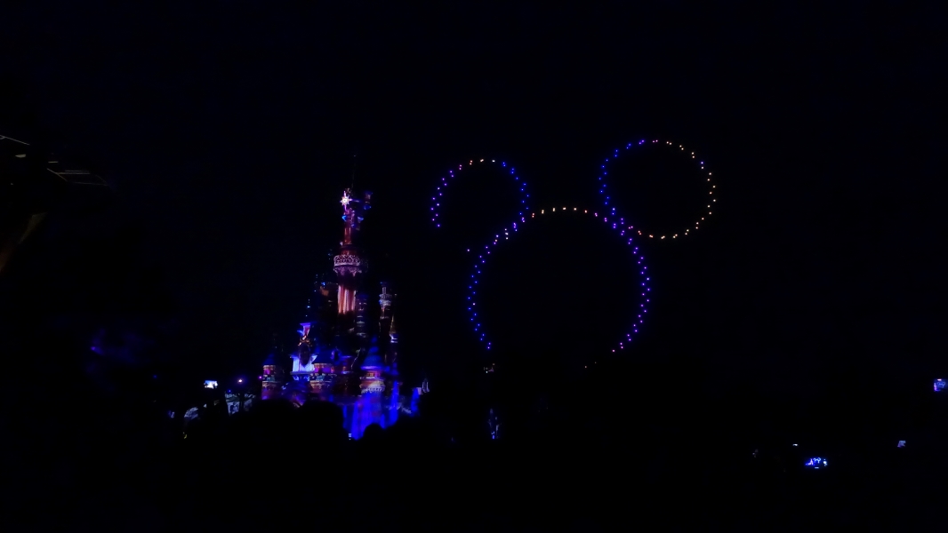 Drones create the outline of Mickey Mouse’s head next to a castle lit at night