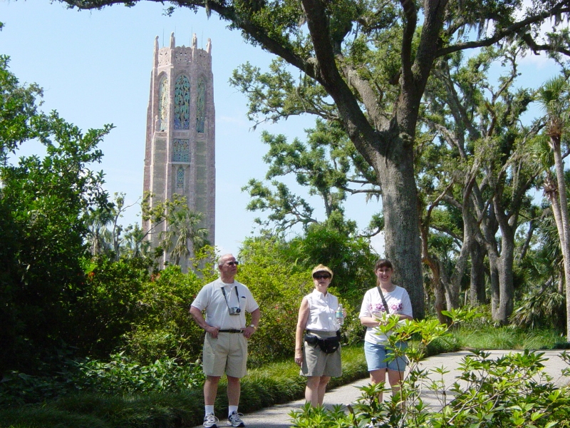 Jim, Gayle, and Julie walk along a path with the Singing Tower rising through the trees behind them