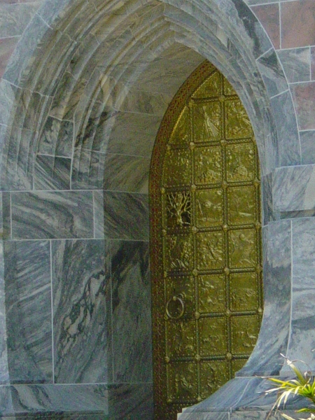 Ornate carved doors set in pink sandstone walls have a tree carved in one of its square panels
