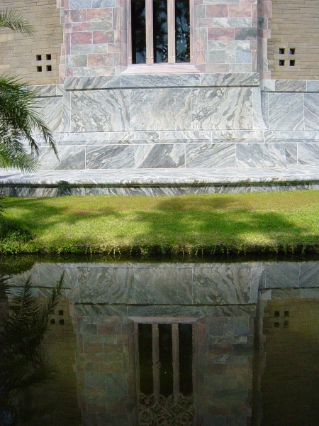 The gray base and pink walls of the tower are reflected in a calm pond