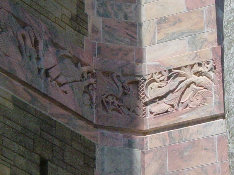 A band of ornate carvings in pink and sand color stone with green highlights