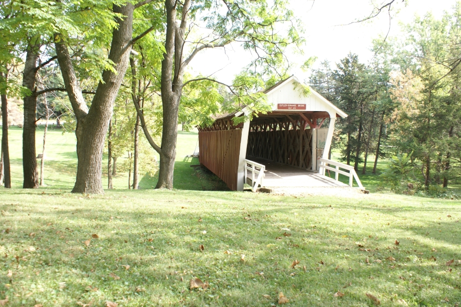 A wooden covered bridge spans a small creek surrounded by trees
