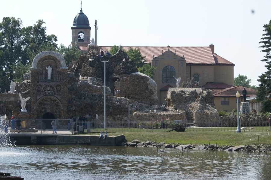 A stone church with a tile roof stands behind a rough surfaced structure with statues around it