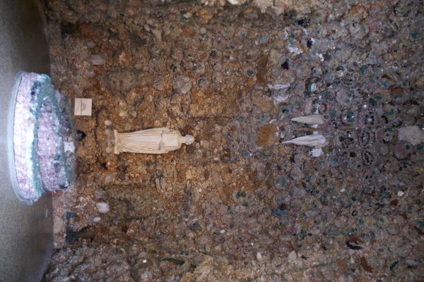 A white statue stands in an enclosure with sparkling stones mixed into the rough walls