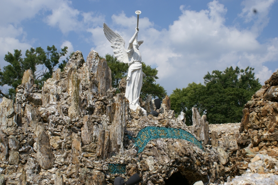 A white angel statue holds a trumpet above amongst rocks forming a cavern