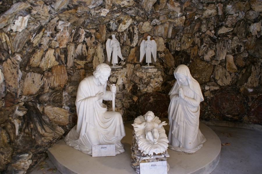 Two kneeling figures on either side of child in a straw filled manger stand in a stone cavern