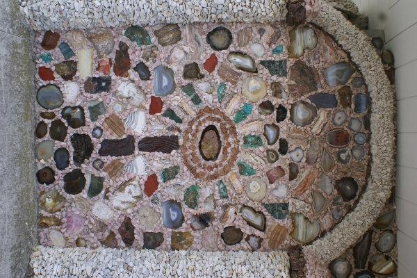 A wall with thin slices of large geodes shows the variety of colors including reds, greens, blues, golds, and grays that can be found in nature