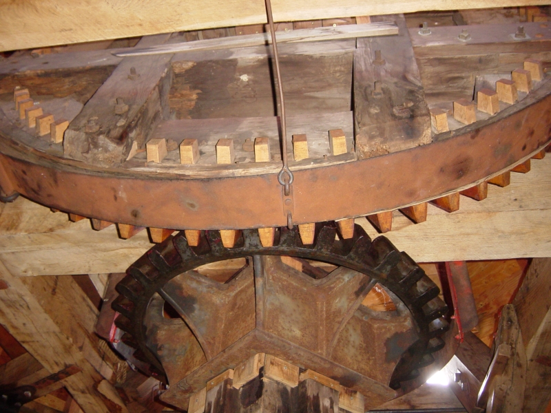 Wooden framing supports large toothed gear wheels meant to transfer the rotation of the windmill blades to a grinding wheel