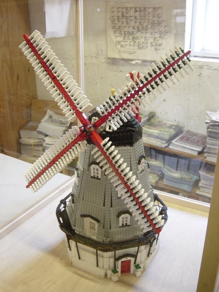 A model of a windmill made from gray and white bricks inside a covered display case