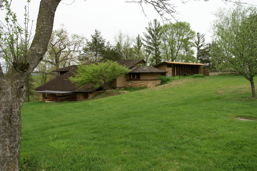 Stone walls come out of the ground as different levels of a house are visible in the slope of a grass covered hillside