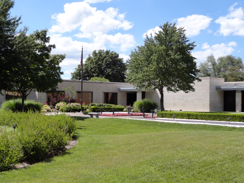 A low white stone building sets amongst green gras and colorful flowers