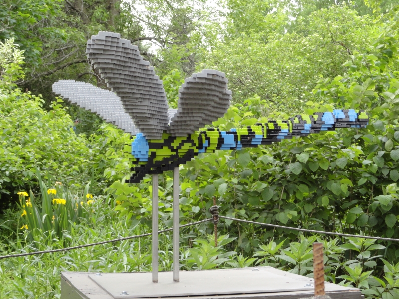 IA LEGO model of a blue and green stripped gray winged dragonfly is surrounded by green foliage