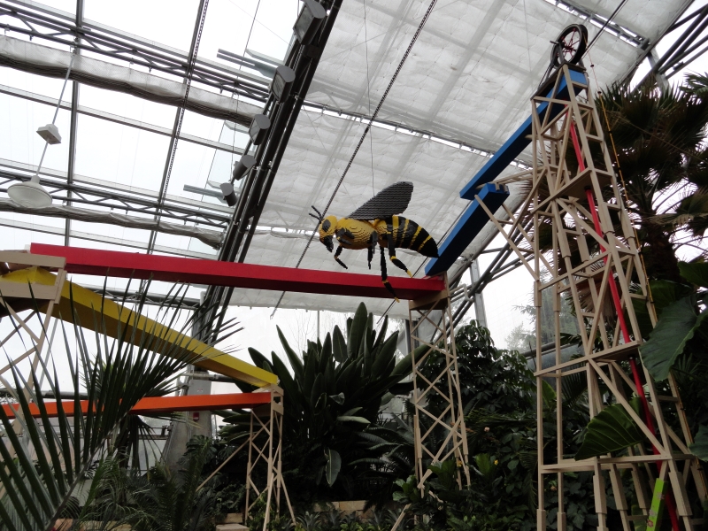 An oversized LEGO wasp is hung from the roof inside a glass building