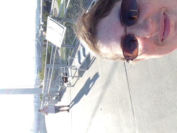 Julie takes a selfie with James in the background taking pictures of a suspension bridge.