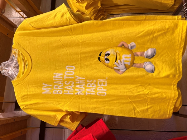 A yellow shirt with a yellow peanut M&M candy says, My brain has too many tabs open