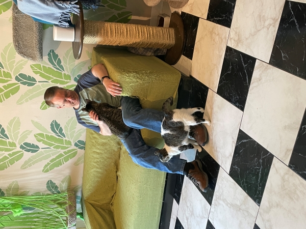 James with one cat in his lap and another rubbing his leg