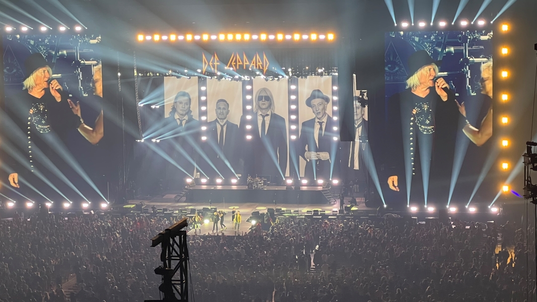 Def Leppard taking a bow with pictures of the band members in 1930’s dress coats and hats on the stage screens