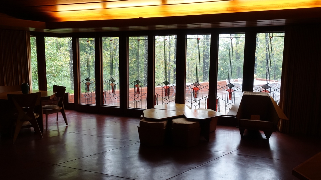 A photo of the living room with a large window wall with many panes, offering a view of the outdoors. The furniture is low-slung and includes a coffee table, chairs, and a sofa. The room has a warm and inviting atmosphere, with soft lighting and natural wood accents.